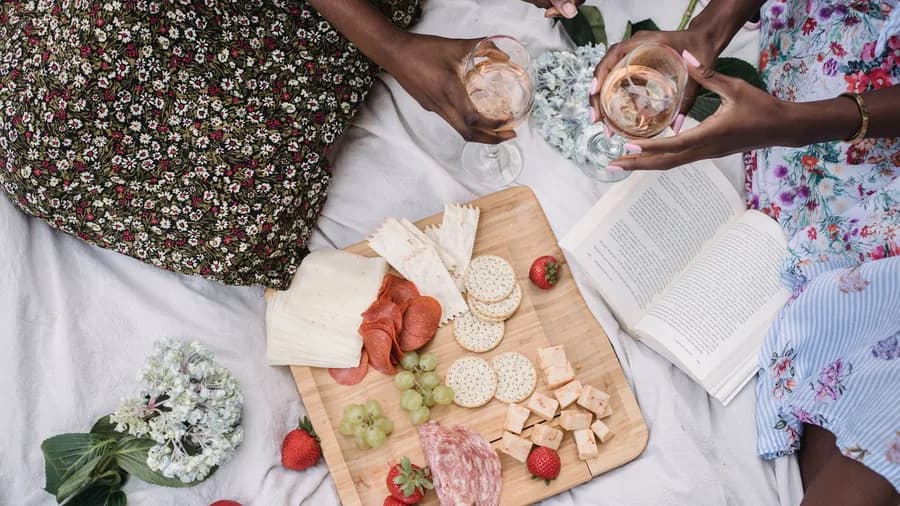 Friends on a picnic blanket around a board of cheese, salami, crackers and strawberries