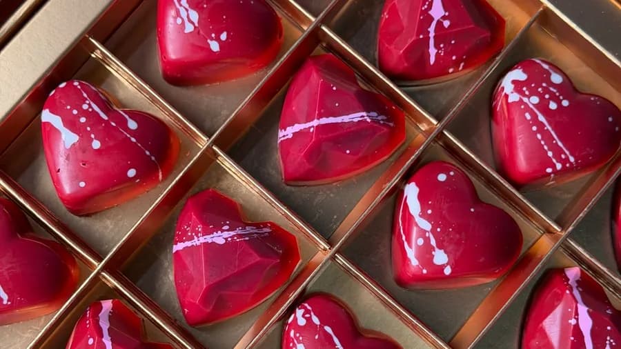 Red heart-shaped bonbons with white splashes in a gold gift box