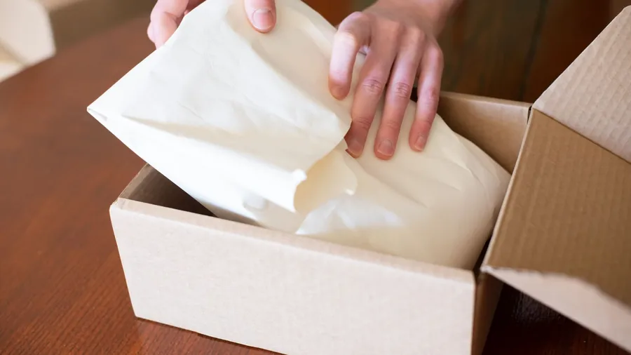Hands folding paper around an order inside a cardboard shipping box