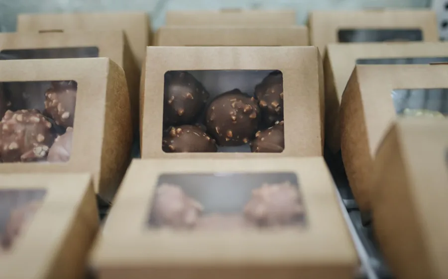 Rows of kraft gift boxes with clear windows, filled with chocolate-covered treats