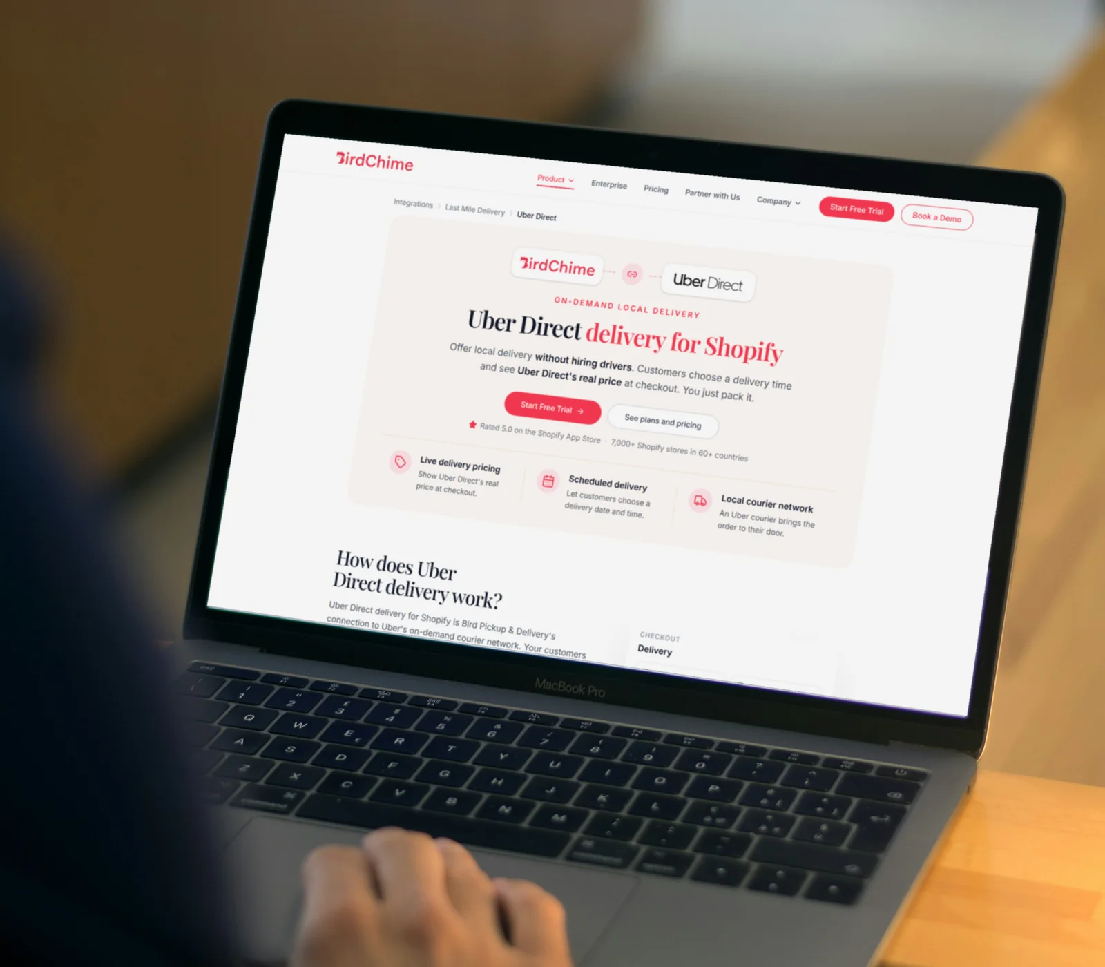 A shop owner at a laptop viewing the BirdChime Uber Direct integration page: Uber Direct delivery for Shopify with live pricing, scheduled delivery and a local courier network